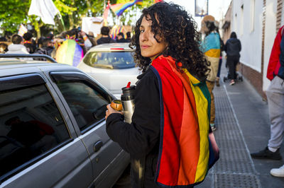 Woman looking at camera while holding a mate with a rainbow flag in an lgbtq pride march.