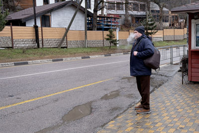 Full length of man smoking cigarette standing on road