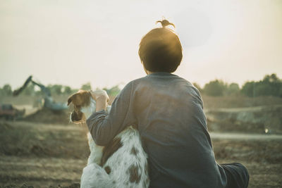 Rear view of woman sitting with dog at construction site against clear sky during sunset