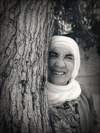 Portrait of a smiling young woman against tree trunk