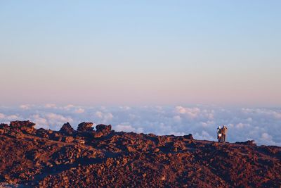 Man standing on rock against sky during sunset