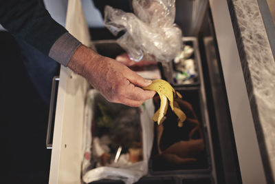 Cropped hand of senior man throwing garbage in dustbin at home