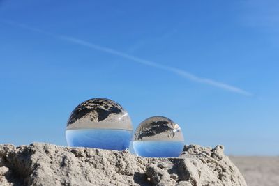 Crystal balls on sand against sky