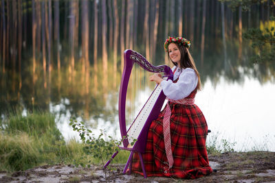 Portrait of young woman playing instrument by lake