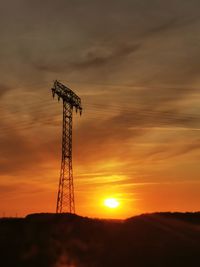 Low angle view of silhouette electricity pylon on field against sky during sunset