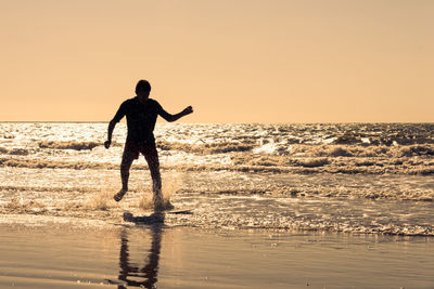 Silhouette man running in sea against clear sky during sunset