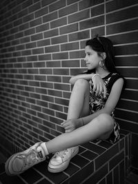 Young woman looking away while sitting against wall