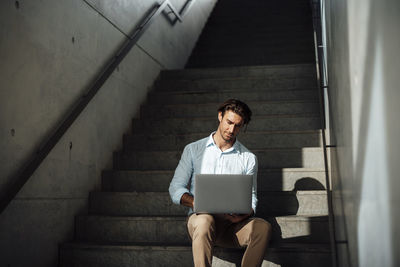 Businessman using laptop sitting on steps