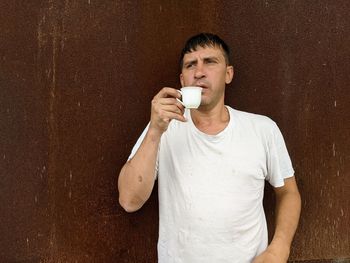 Portrait of young man drinking glass against wall