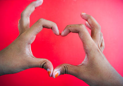 Close-up of hands holding heart shape against red background