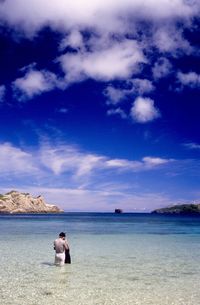 Rear view of couple sitting on beach against sky