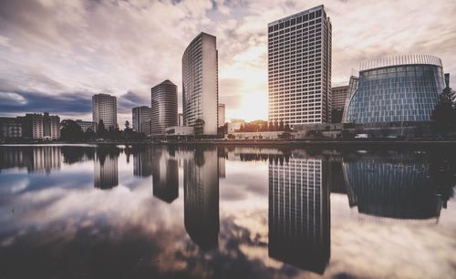 Reflection of buildings in city against cloudy sky during sunset