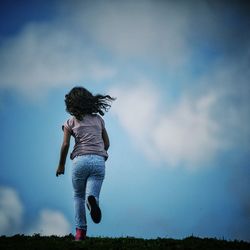 Full length rear view of girl running on field against sky