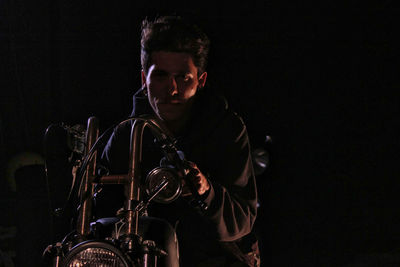 Portrait of young man sitting on motorcycle against black background