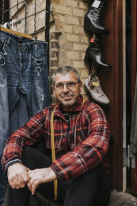 Portrait of smiling male owner sitting outside clothing store