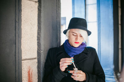 Close-up of young woman preparing electronic cigarette by column