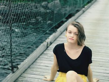 Portrait of young woman looking down while sitting on bridge