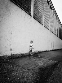 Full length of boy standing on footpath against wall