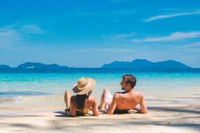 Rear view of woman sitting at beach against sky