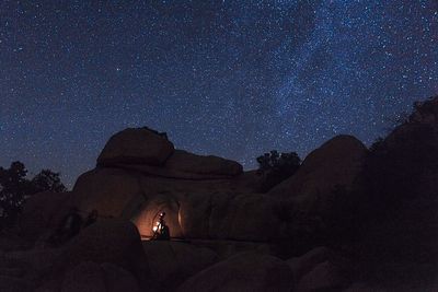 Silhouette of photographer on rocks against sky at night