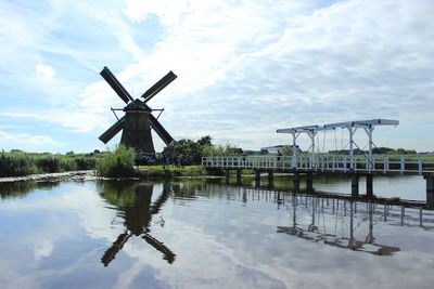 Traditional windmill by lake against sky
