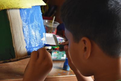 Close-up portrait of boy painting cardboard house at home