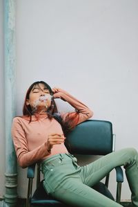 Woman sitting on chair against wall