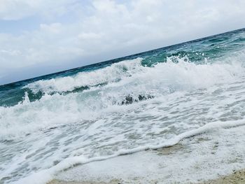 Scenic view of sea waves splashing on shore against sky