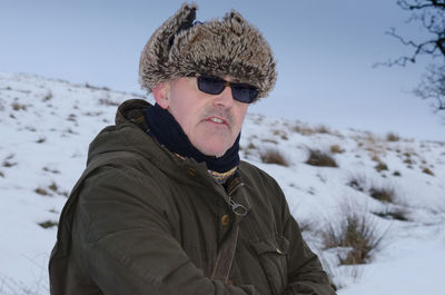 Man wearing fur deerstalker hat while standing on snowy field