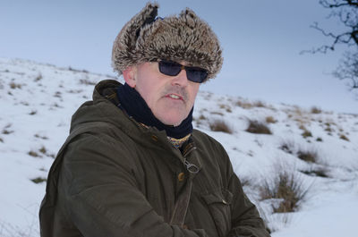 Man wearing fur deerstalker hat while standing on snowy field