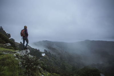 Woman standing on mountain against cloudy sky