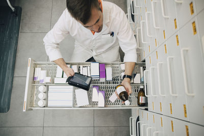 High angle view of pharmacist checking medicine bottle with digital tablet at store