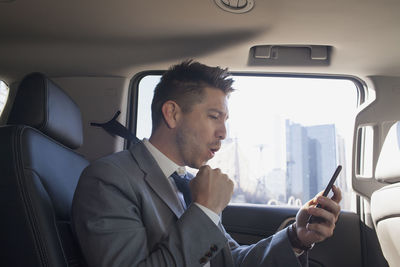 Young businessman looking at smartphone sitting in car service limousine