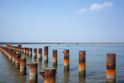 Wooden posts in sea against sky