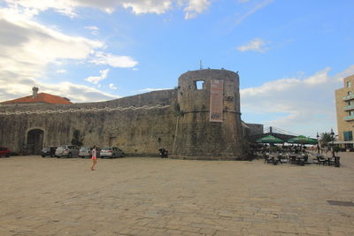 Tourists in front of historical building against cloudy sky