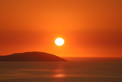 Scenic view of small island in sea against romantic sky at sunset