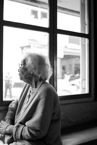 Old lady looking away while sitting on window at home