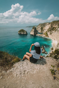 Man standing on rock by sea against sky