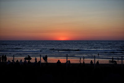 Silhouette people at beach against sky during sunset