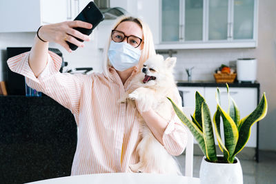 Woman wearing mask talking on video call with dog at home