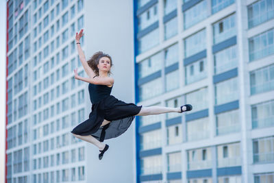 Full length of young woman jumping against building