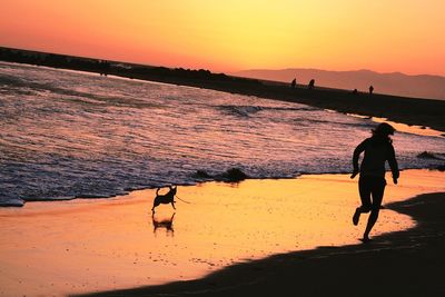 Silhouette people walking on beach against orange sky