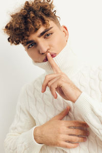 Young man with finger on lips standing against white background