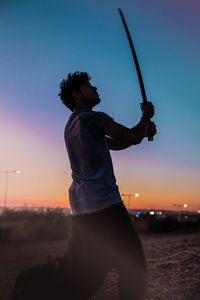 Side view of man standing on beach against sky at sunset