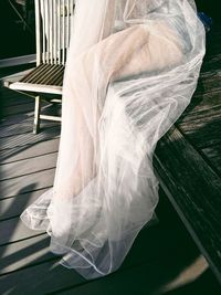 Low section of woman sitting on wooden bench with white tulle netting
