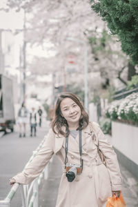 Portrait of smiling woman with camera standing on footpath