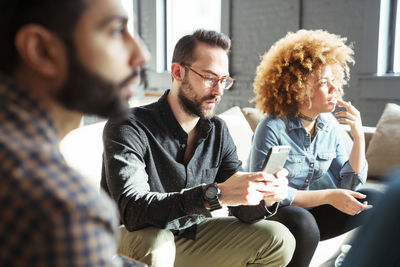 Businessman using mobile phone while sitting with colleagues in office