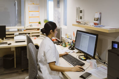 Side view of female healthcare worker using desktop pc at hospital