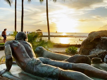 Rear view of men on rock by sea against sky during sunset