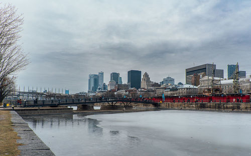 Buildings by river against cloudy sky